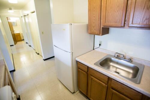 An empty kitchen with a refrigerator and sink.